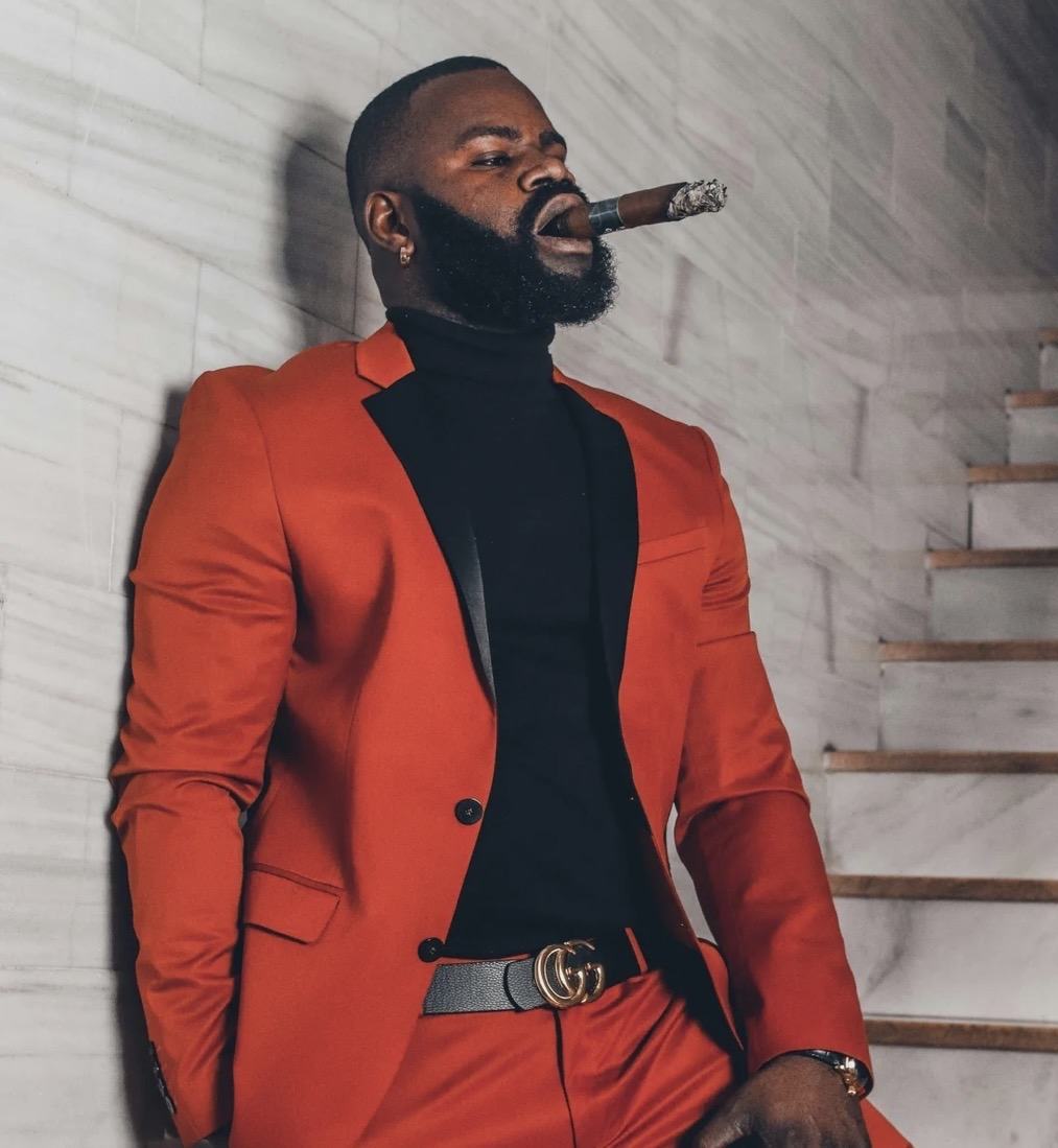 A guest in a red suit and black turtleneck standing beside a pale marble stair wall